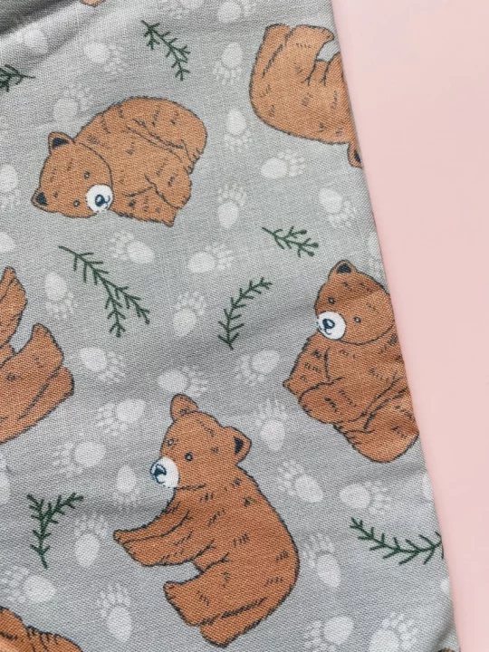Piece of fabric on pink backdrop. Fabric is pale grey with lighter grey paw prints and leaf motif with large pale brown bear cubs