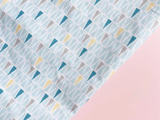 Piece of fabric on pink backdrop with pale blue interlocking triangles outlined with white. Random triangles are yellow, pale grey or darker blue