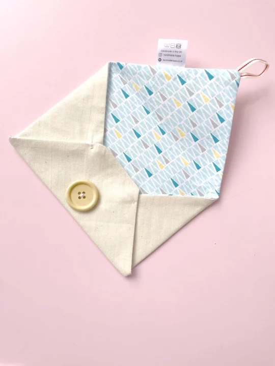 Finished fabric envelope on pink backdrop, envelope is open to show the inside of the envelope which has a blue triangle design