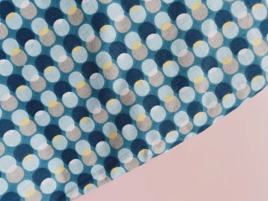 Piece of fabric on pink backdrop. Fabric is blue with overlapping darker blue, yellow, pale great and pale blue in lines