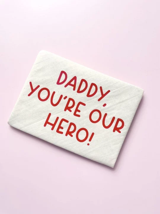 closed finished envelope on pink background showing red text saying "Daddy, you're our hero!" in capital letters