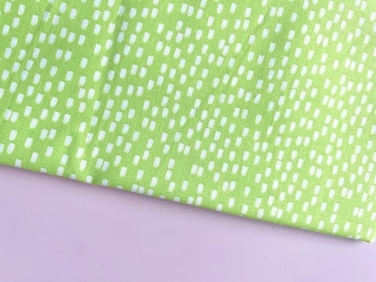 Piece of fabric on pink backdrop. Fabric is bright green with brushstroke like irregular dash design