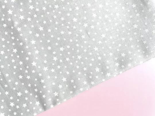 Piece of fabric on pink backdrop. Fabric is pale grey with scattered white stars in different sizes