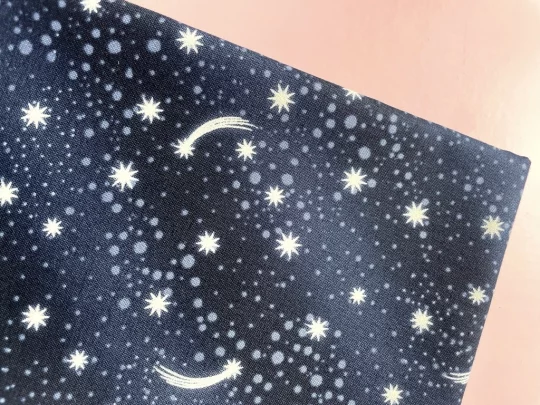 Piece of fabric on pink backdrop. Fabric is navy blue with shooting star design with scattered pale grey circles in different sizes