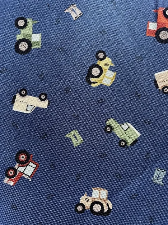 Piece of fabric on pink backdrop. Fabric is dark blue with tractors and jeeps in different colours
