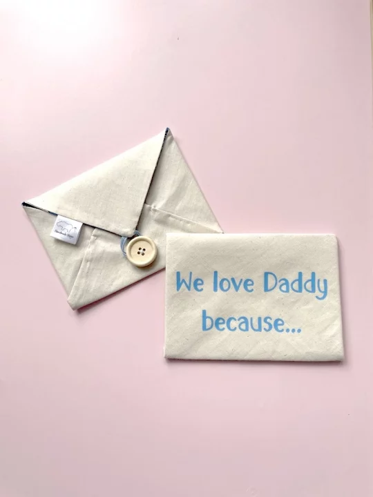 wo closed finished envelopes, slightly overlapped on pink background. One envelope is closure side facing up and the envelope personalisation side up says "We love Daddy because..." in light blue text.