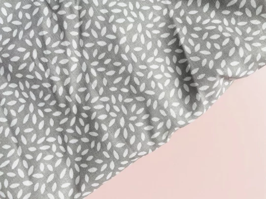 Piece of fabric on pink backdrop. Fabric is pale grey with scattered white rice shaped motif