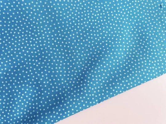 Piece of fabric on pink backdrop. Fabric is blue with irregular small white spots